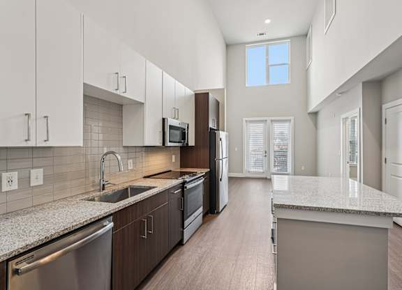 A modern kitchen with a large island and stainless steel appliances. A large bedroom with a ceiling fan and a window s. a large, high ceiling, apartment that has two floors, is a modern loft, and in atlanta