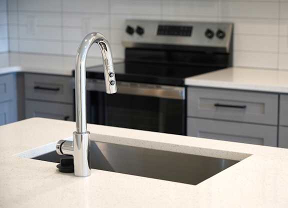 A kitchen sink with a chrome faucet. and stain gray and white cabinets