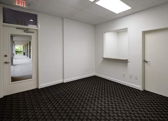 A room with a black carpet and white walls with a door on the left.