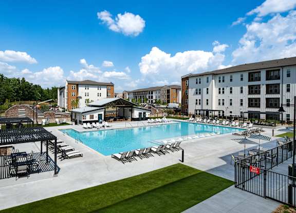 A large swimming pool surrounded by lounge chairs and a fence.