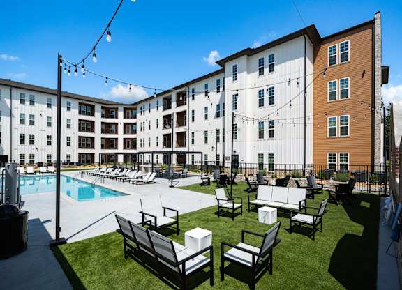 A sunny day at the poolside with chairs and a building in the background.