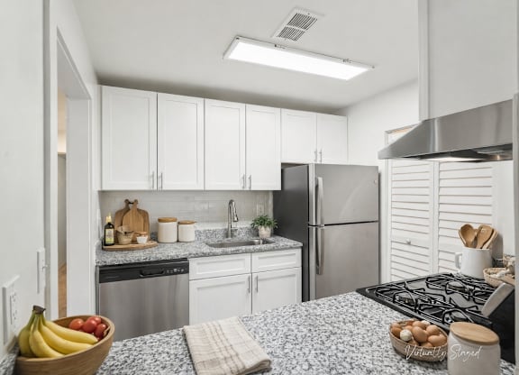 A kitchen with a refrigerator, sink, and a bowl of fruit on the counter.
