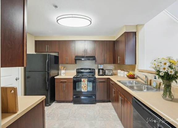 A kitchen with a black refrigerator, black oven, and brown cabinets.