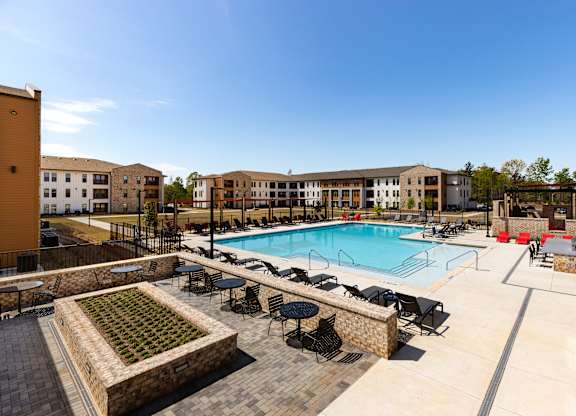 A large swimming pool surrounded by chairs and tables in a sunny outdoor area.