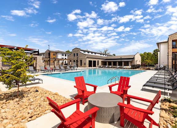 A pool surrounded by red chairs and tables.