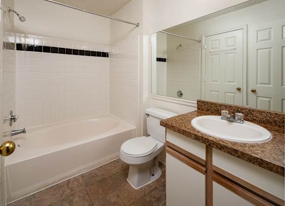 A white bathroom with a brown granite counter top.
