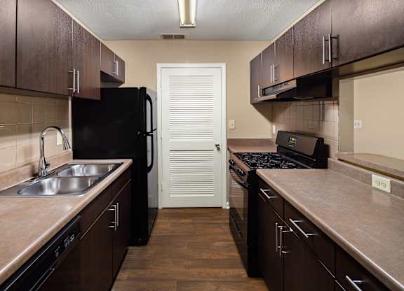 A kitchen with dark brown cabinets and a black fridge.
