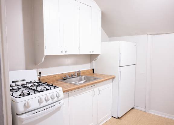 A white kitchen with a stove, sink, and refrigerator.