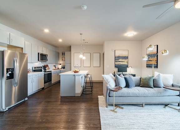 a living room with a couch and a kitchen with stainless steel appliances at Parkside at Littleton Village, Littleton