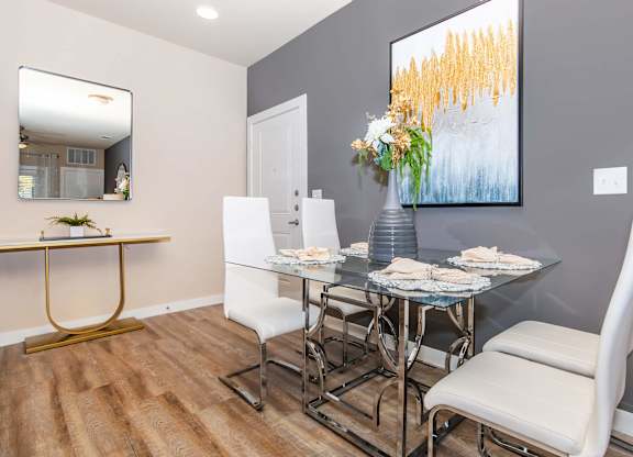 A dining room with a glass table and white chairs.