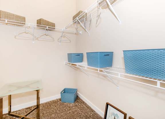 A room with a white wall and a shelf with clothes hangers and baskets.