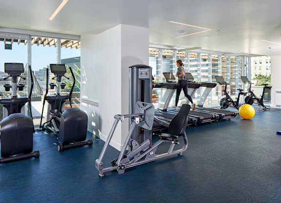 A gym with a row of treadmills and a woman working out.