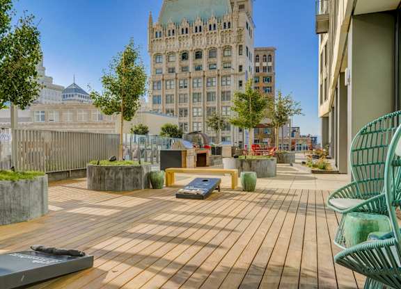 A wooden deck with a green chair and a bench in the foreground with a building in the background.
