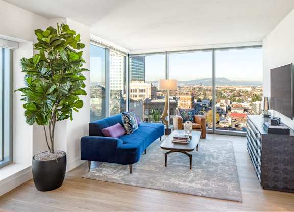 A living room with a blue couch and a large window overlooking the city.