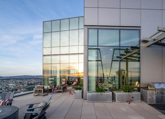 A modern building with a glass facade and a rooftop terrace with seating and plants.