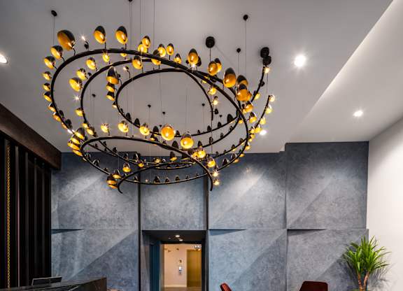 A modern chandelier with circular lights hangs from the ceiling in a room with grey walls and a wooden floor.