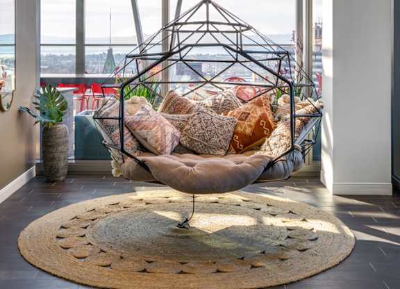 A hanging chair is suspended from a metal frame in a room with a view of the ocean.