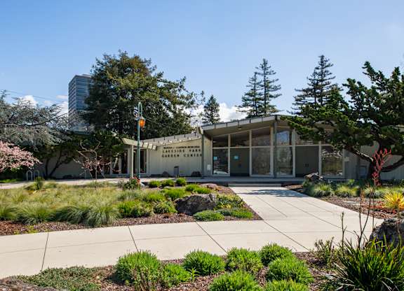 A building with large windows and a sidewalk, with lots of bushes.