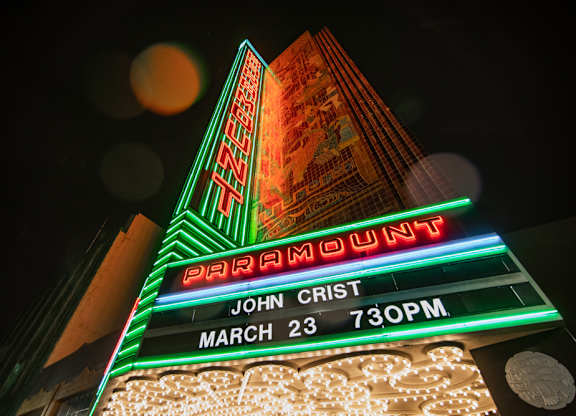 A brightly lit marquee sign for a show by John Crist on March 23 at 7:30 PM.