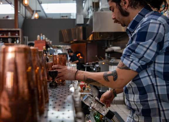A man in a plaid shirt is pouring a drink from a tap.
