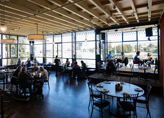 A group of people are sitting at tables in a restaurant with a view of the outside.