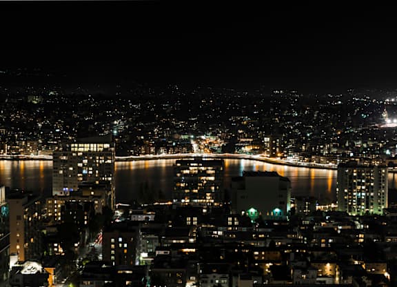 A cityscape at night with lights from buildings and a body of water.