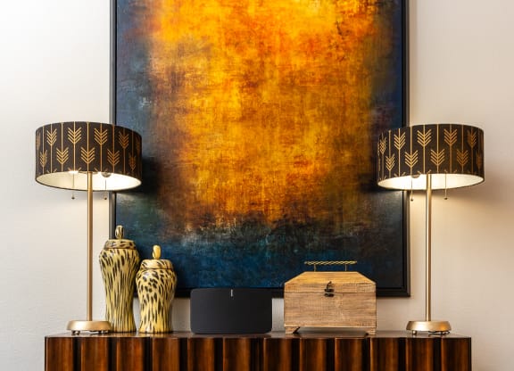 a living room with a desk with two lamps and a painting