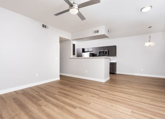 an empty living room with a ceiling fan and a kitchen
