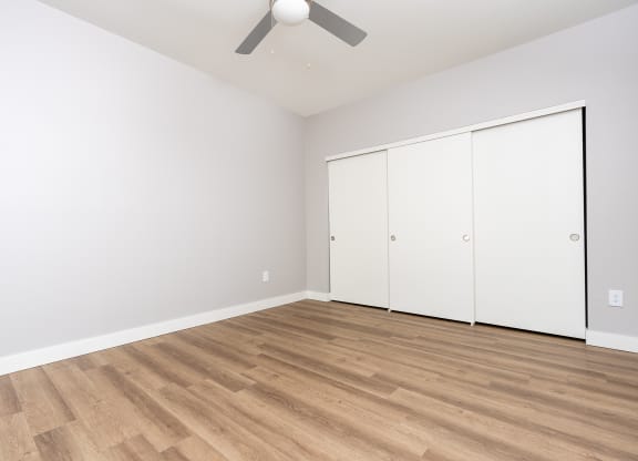 a living room with white walls and wood flooring and a ceiling fan