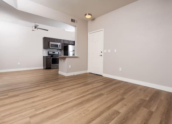 an empty living room with wood flooring and a kitchen