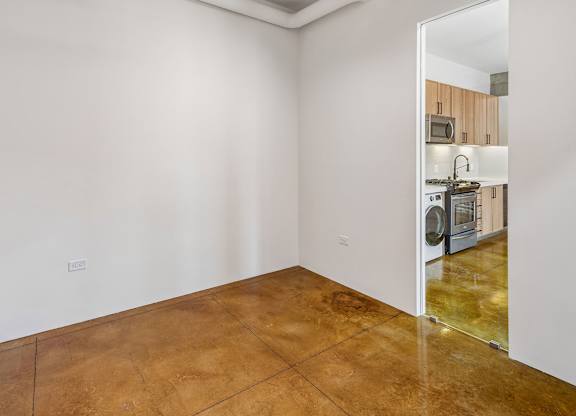 A kitchen with white walls and a brown floor is visible through an open door.