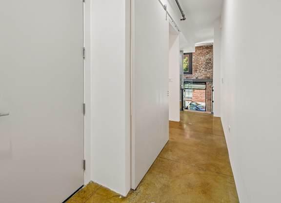 A long hallway with a white door on the left and a brick wall in the distance.