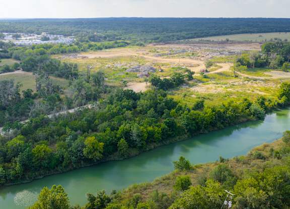 A river flows through a green forest with a town in the distance.