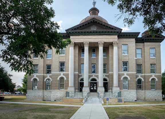 A large, stately building with a dome and columns stands under a clear sky.