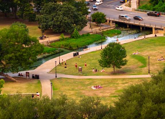 A park with people sitting on the grass and a river running through it.