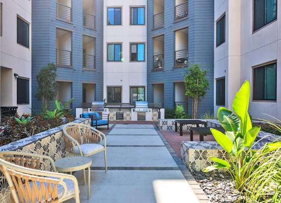 A courtyard with chairs and plants in front of apartment buildings.