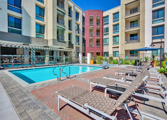 A pool area with sun loungers and a red building in the background.