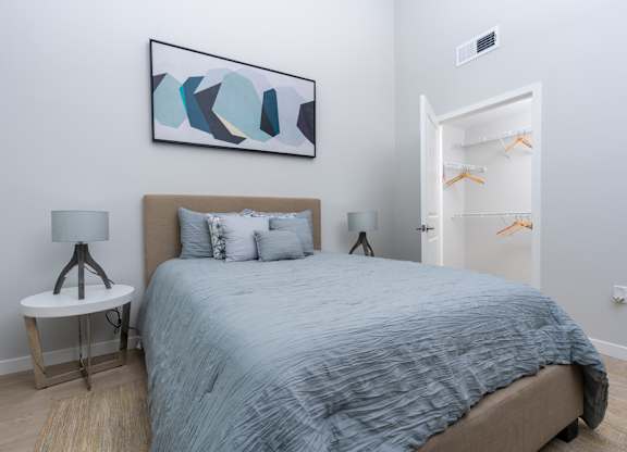 A bedroom with a bed, a side table with a lamp, and a painting on the wall.