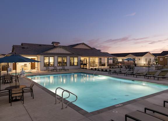 A swimming pool surrounded by lounge chairs and umbrellas in front of a building.