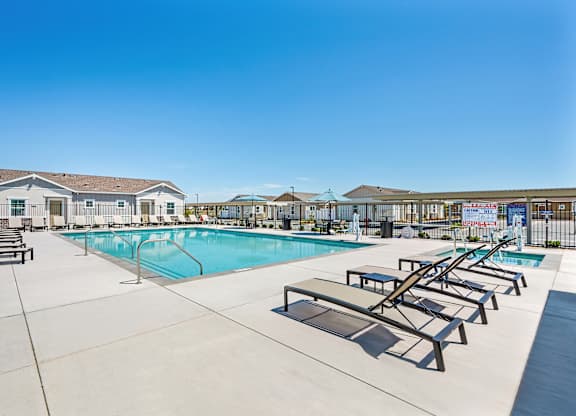 A large outdoor swimming pool with sun loungers and a building in the background.