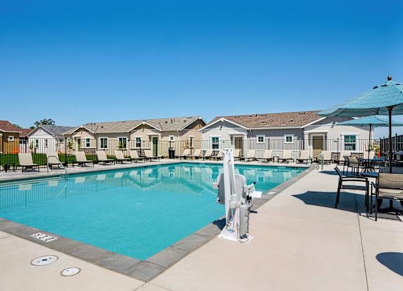 A swimming pool surrounded by lounge chairs and umbrellas with a building in the background.