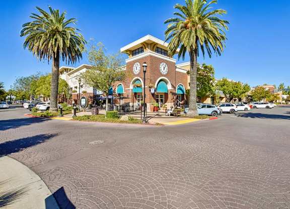 A clock tower is in front of a building with palm trees.