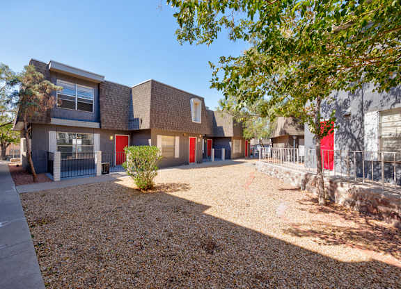 Desert Peaks building with a red door is surrounded by a gravel area and trees.