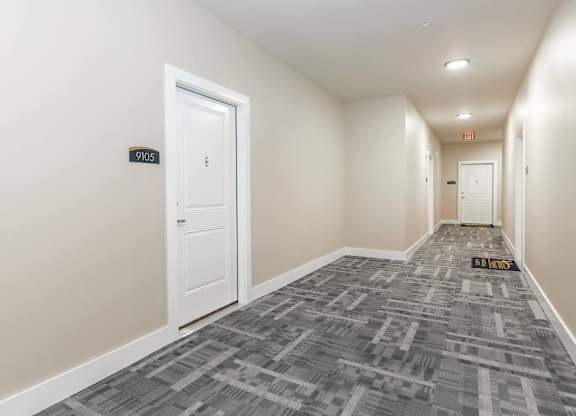 A hallway with a carpeted floor and a door on the left.