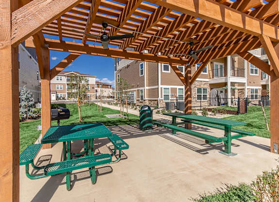 A wooden pergola with green picnic tables is in the foreground of a residential area.