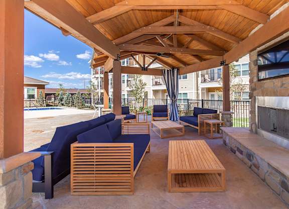 A wooden patio with a stone fireplace and blue couches.