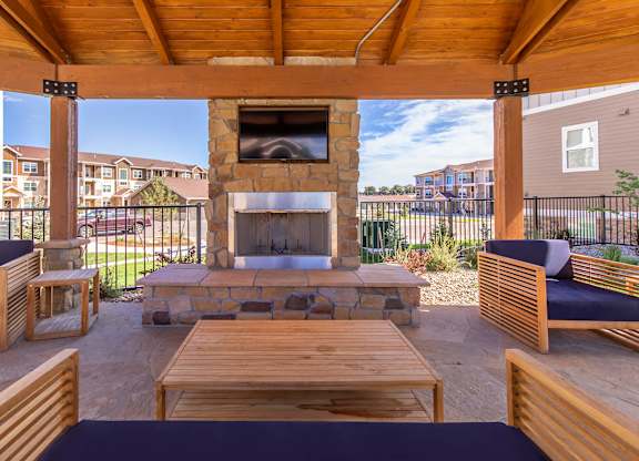 A wooden patio with a stone fireplace and seating area.