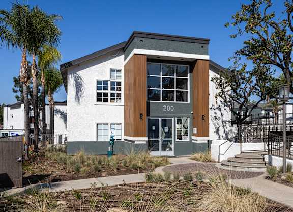 A modern building with a white facade and a brown door is surrounded by palm trees at Verandas Apartments, California