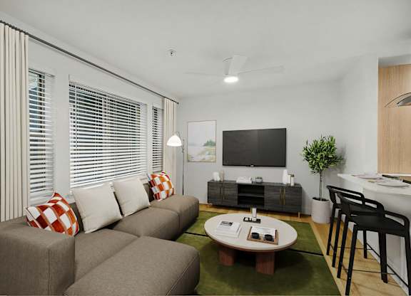 A living room with a grey couch, a green rug, a wooden coffee table, and a television.