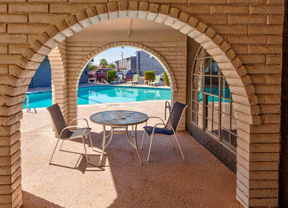 A table and chairs are set up on a patio with a pool in the background.